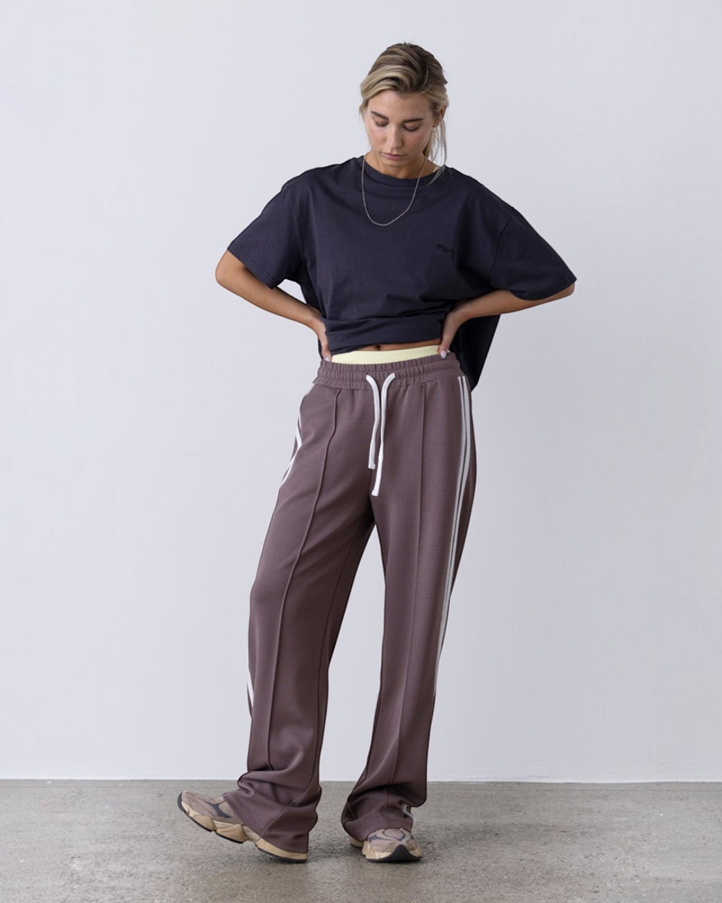 Model trägt taupefarbene greenyogashop Lounge-Trackpants mit weitem Bein, elastischem Bund und Herringbone-Seitenstreifen