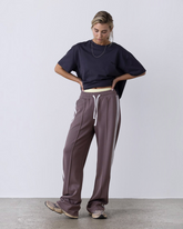 Model trägt taupefarbene greenyogashop Lounge-Trackpants mit weitem Bein, elastischem Bund und Herringbone-Seitenstreifen