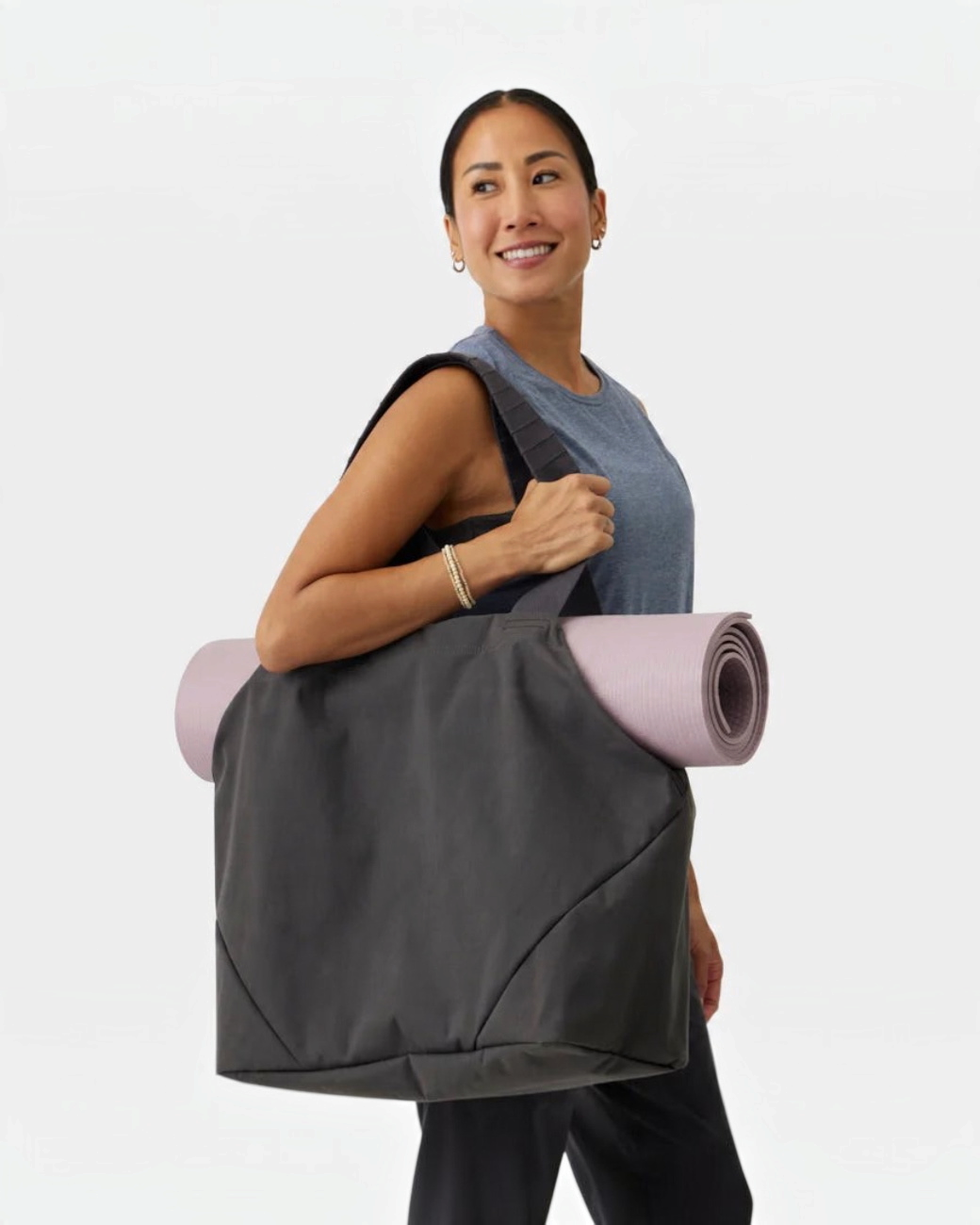 greenyogashop Kosha Carryall Tragetasche in Pearl mit Yogamatte über der Schulter einer lächelnden Frau
