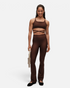 Model trägt dunkelbraune greenyogashop Flare High Waist Leggings mit ausgestelltem Bein und passendem Sport-BH