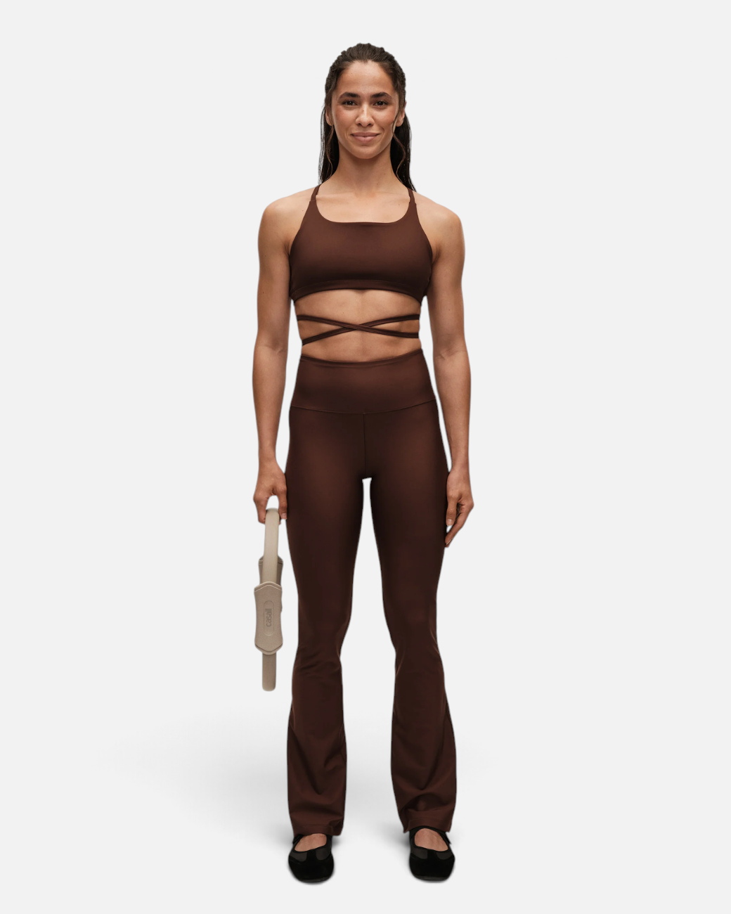 greenyogashop Flare High Waist Hose in Dunkelbraun, getragen von einer Frau mit passendem Sport-BH und Pilates-Ring