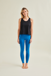 Woman wearing a black sports tank top made from GOTS certified organic cotton and eco-friendly blue leggings