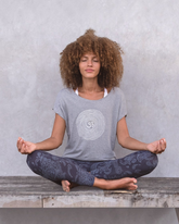 greenyogashop T-Shirt OM aus grauer Biobaumwolle mit Om-Print, getragen von einer Frau in Meditationshaltung